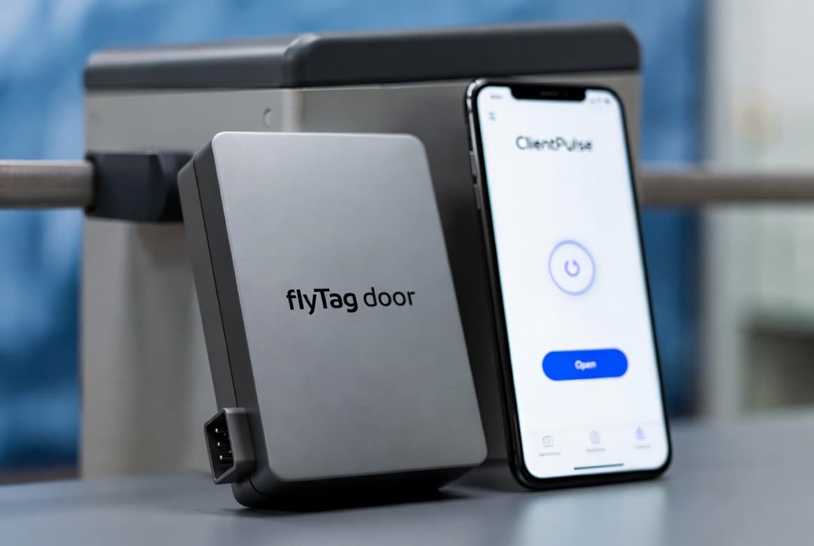 flyTag Door — открытие ворот со смартфона Контроллер flyTag Door на приводе шлагбаума рядом со смартфоном с приложением ClientPulse и кнопкой открытия